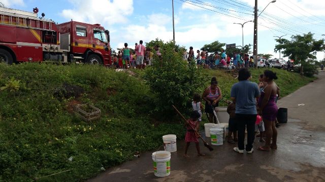 Populares enchem baldes com água do carro do Corpo de Bombeiros acionado para apagar fogo na pista